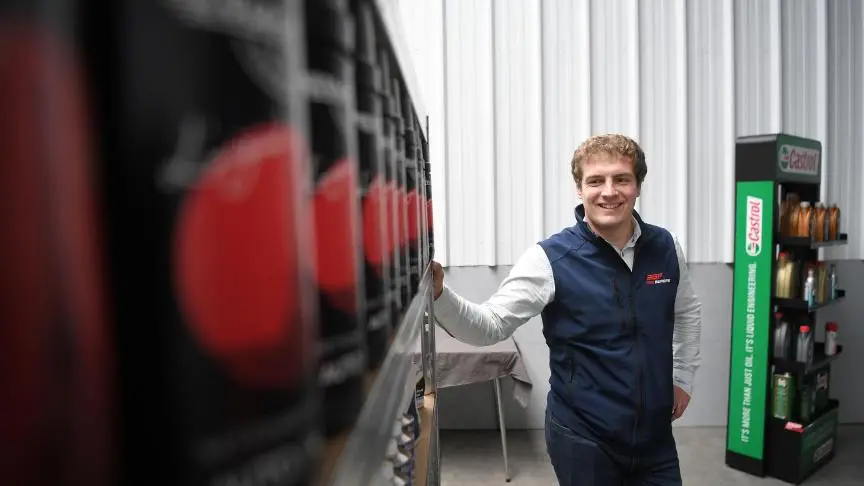 Collaborateur souriant devant des rayons d'huile moteur et un présentoir Castrol dans l'entrepôt du client