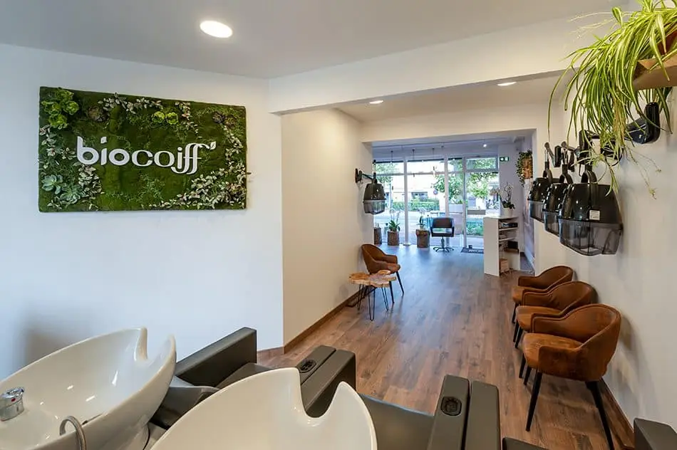 Intérieur du salon Biocoiff avec bacs à shampoing, fauteuils cognac et mur végétal, un salon de coiffure bio