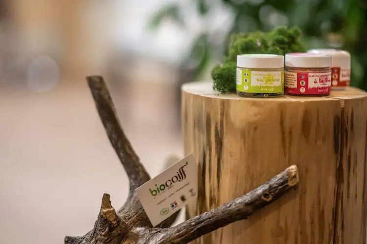 Pots de soins capillaires naturels posés sur un rondin de bois avec étiquette de la marque de coiffure bio